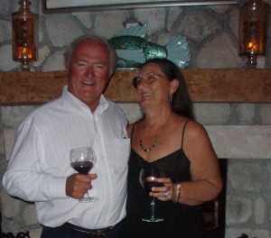 Rick and Charlene holding wine glasses in front of the dining room fire place