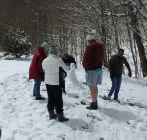 Six people surrounding a small snow man