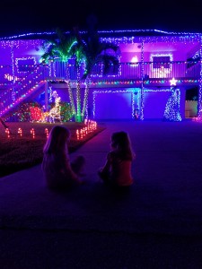 Two-story home with many Christmas lights displayed and two children sitting in front