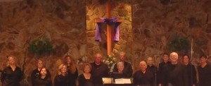 Choir members dressed in black standing in choir loft in front of cross