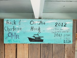 A sea green sign with black letterin saying Rick & Charlene, On The Hook - with a drawing of the boat, and the years 2012, 2013, 2014, 2015, 2016, 2017, 2018