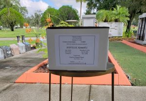 a white cardboard box on a stand with a label stating that Ken Sosville's ashes are inside