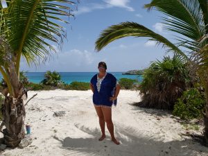 Woman wearing beach cover-up on white sand framed by palm trees with blue ocean in the background