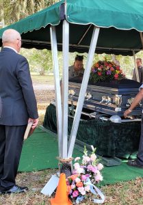 Casket under a canopy with attendants and flowers