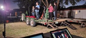 5 people on a flat-bed trailor decorated for Christmas preparing to sing.