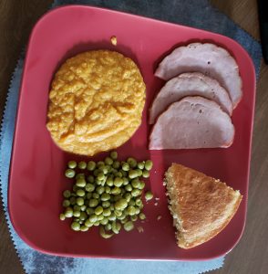 Red dinner plate with Ham, mashed sweet potatoes, peas and corn bread