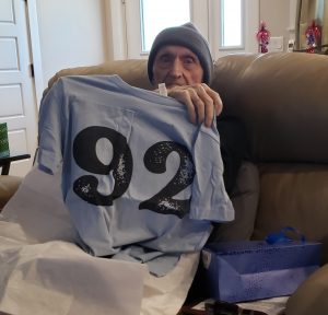 Dad holding up a powder-blue T-shirt that says 92