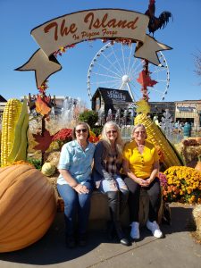 Charlene, Rene and Jackie sitting on a bench surrounded by Fall harvest decorations