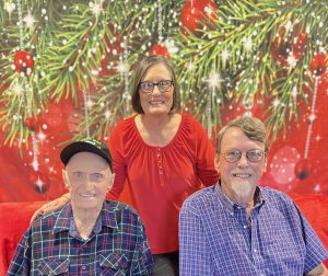 Dad, Charlene and Rick in front of a Christmas backdrop