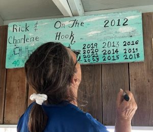 Charlene adding 2023 to the On The Hook sign which was created in 2012 and updated since then