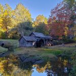 Mill with waterwheel with trees with fall color behind and a reflecting pond in front