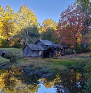 Mill with waterwheel with trees with fall color behind and a reflecting pond in front
