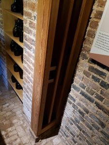 Wooden frame with spaces for wine bottles to travel up to the next floor