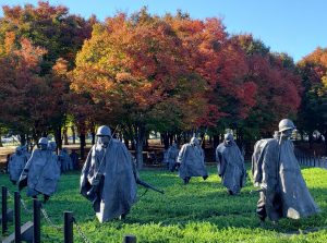 Bronze soldiers walking through the grass with colorful trees behind