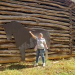 Jackie standing in front of a log barn with a larger-than-life sized cut-out of a black horse