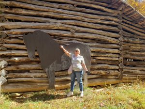 Jackie standing in front of a log barn with a larger-than-life sized cut-out of a black horse