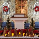 Sanctuary with Manger scene in the foreground with lit trees and wreaths in the background